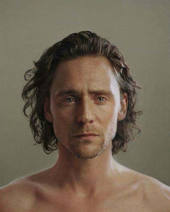 A pensive man with long hair and stubble looks directly at the camera against a neutral background.