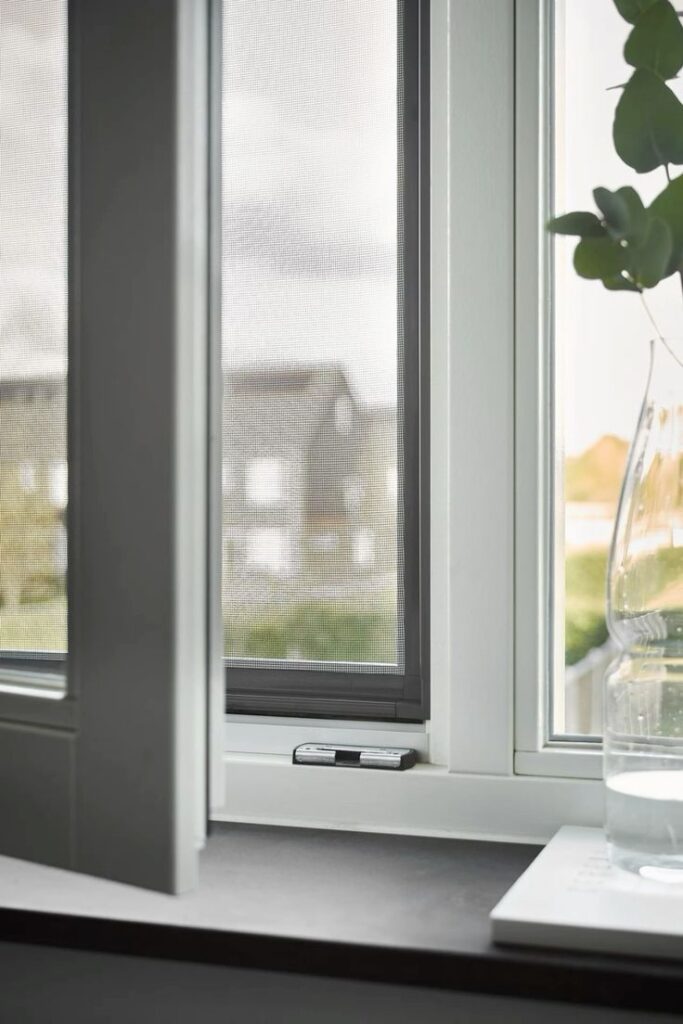 Modern open window with screen, view of suburban neighborhood outside, glass vase with water on the windowsill.