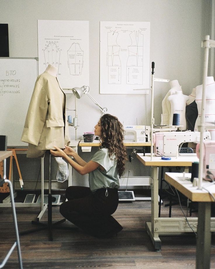 Fashion designer adjusting a beige jacket on a mannequin in a sewing studio with patterns and sewing machines.