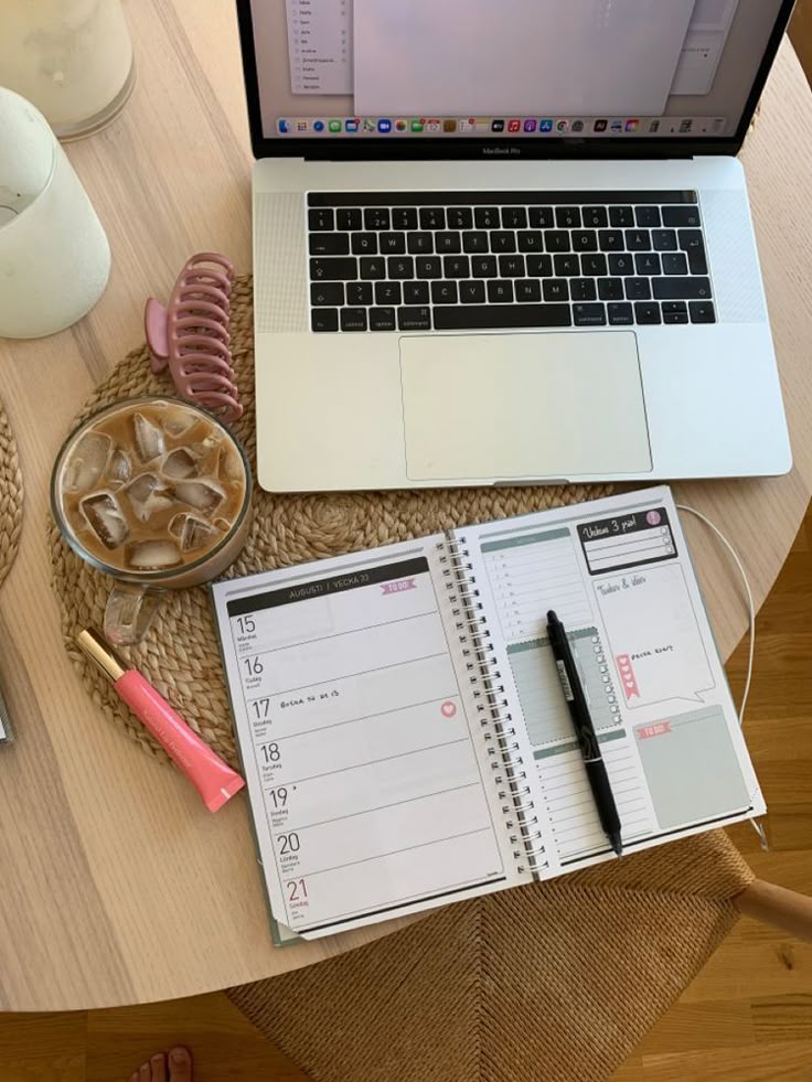 Open laptop on desk with planner, iced coffee, and pink pen; organized workspace for productivity and planning.