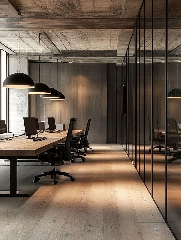 Modern office with wooden desks, ergonomic chairs, and pendant lights, featuring a minimalist design and glass partitions.