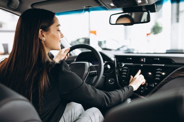 Woman driving car and using touchscreen dashboard for navigation and controls.