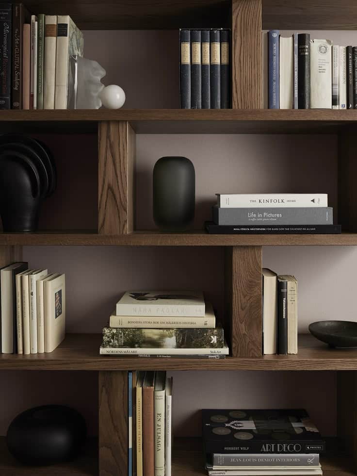 Wooden bookshelf with assorted books, minimalist decor, and sculptures, creating a cozy and stylish home library vibe.