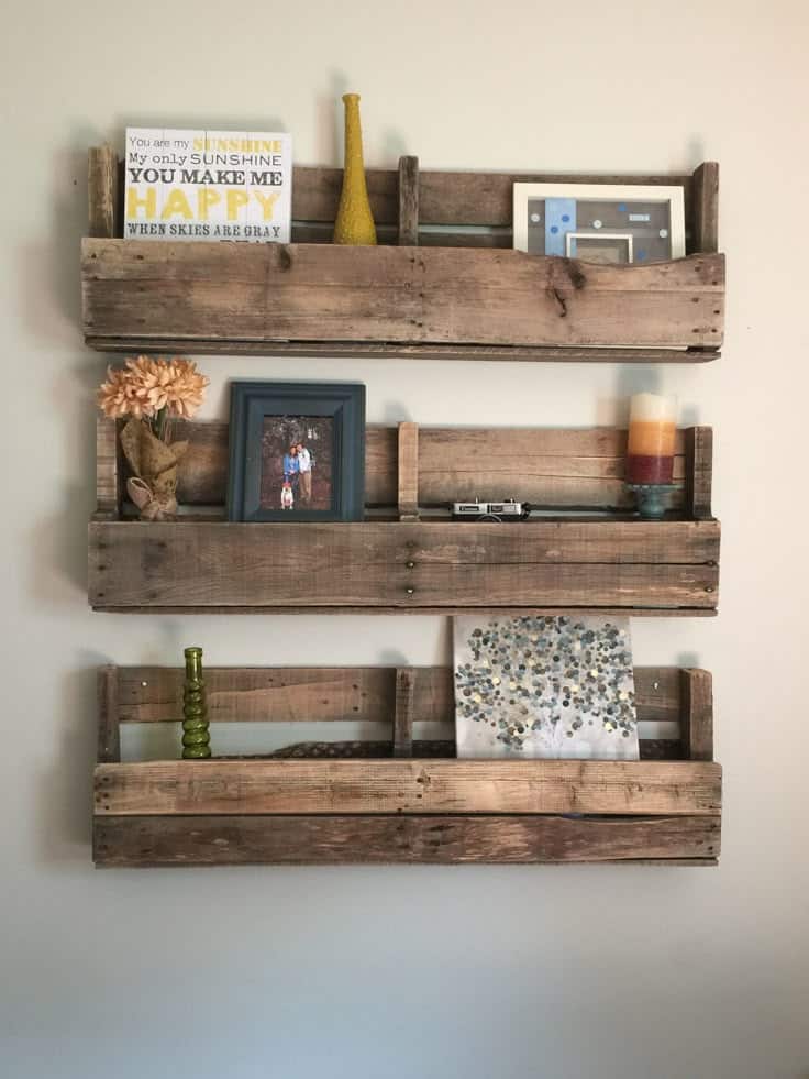 Rustic wooden pallet shelves displaying decor, art, and framed photos against a beige wall. Cozy home interior style.