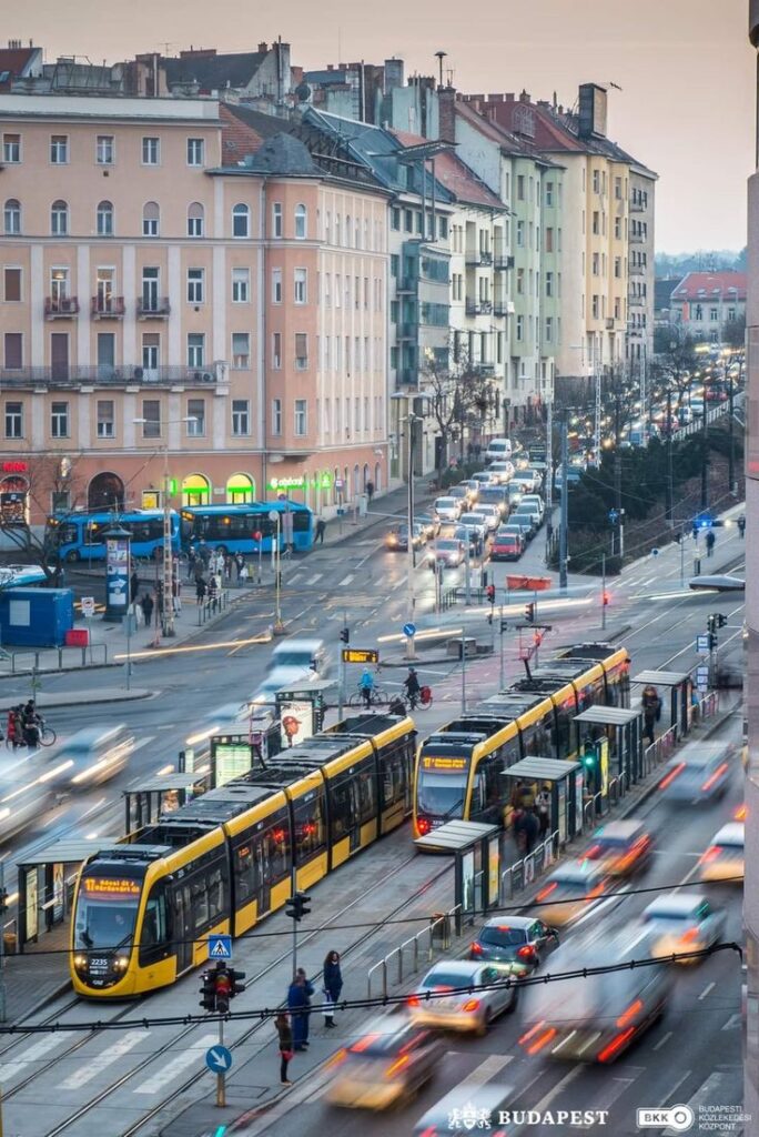 Busy Budapest street with yellow trams, cars, and historic buildings during a vibrant evening commute.