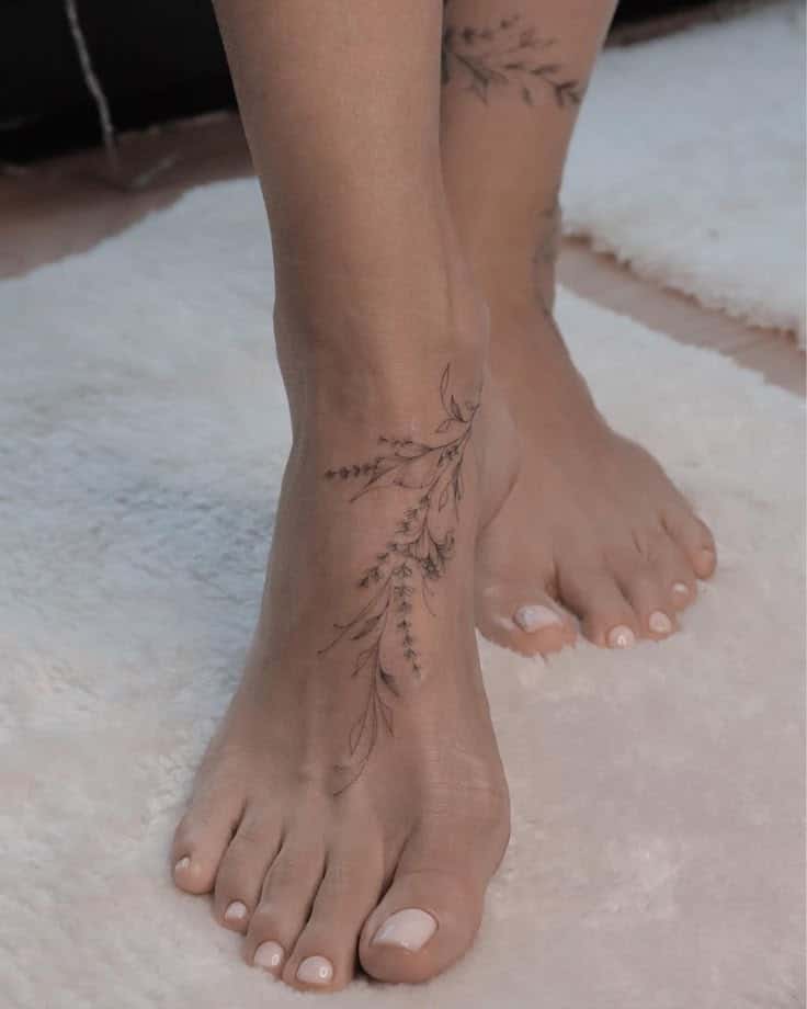Delicate floral ankle tattoo on woman's feet with light pink nail polish, resting on a soft white rug.