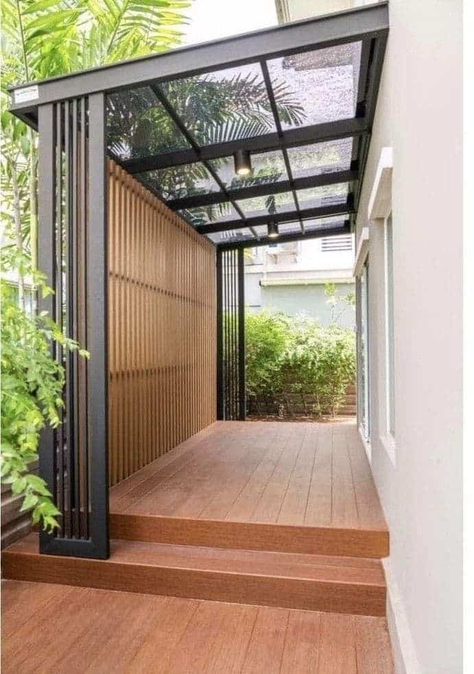 Modern covered patio with wooden flooring and glass roof, surrounded by lush greenery.