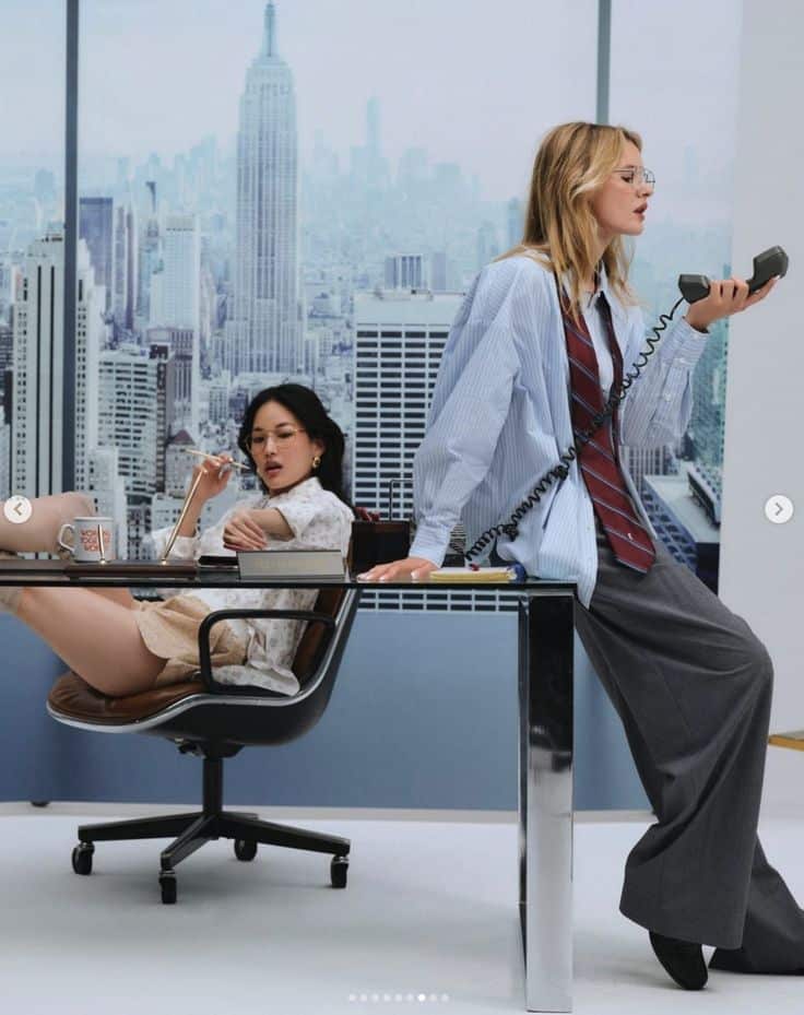 Screenshot Two women in a stylish office setting with a city skyline backdrop, engaged in a business conversation. | Sky Rye Design Two women in a stylish office setting with a city skyline backdrop, engaged in a business conversation.