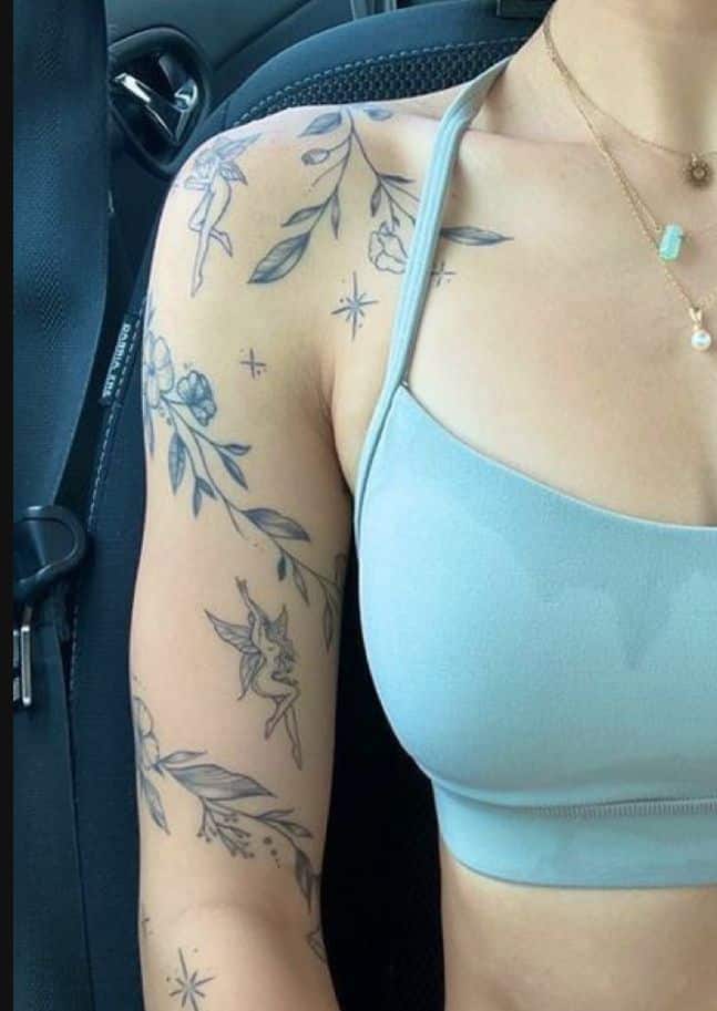 Woman's shoulder adorned with floral and fairy tattoos, wearing a light blue top in a car seat.