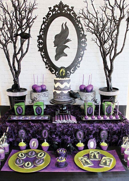 Purple and black themed dessert table with Halloween decorations, featuring cakes, treats, and eerie tree silhouettes.