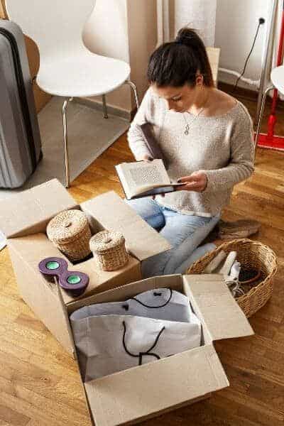 10 Pro Tips On How To Declutter Before A Move _ ThePlainSimpleLife Woman unpacking boxes while reading a book in a cozy room. | Sky Rye Design Woman unpacking boxes while reading a book in a cozy room.