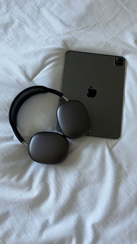 Black headphones and a sleek tablet with a logo placed on a white fabric surface.