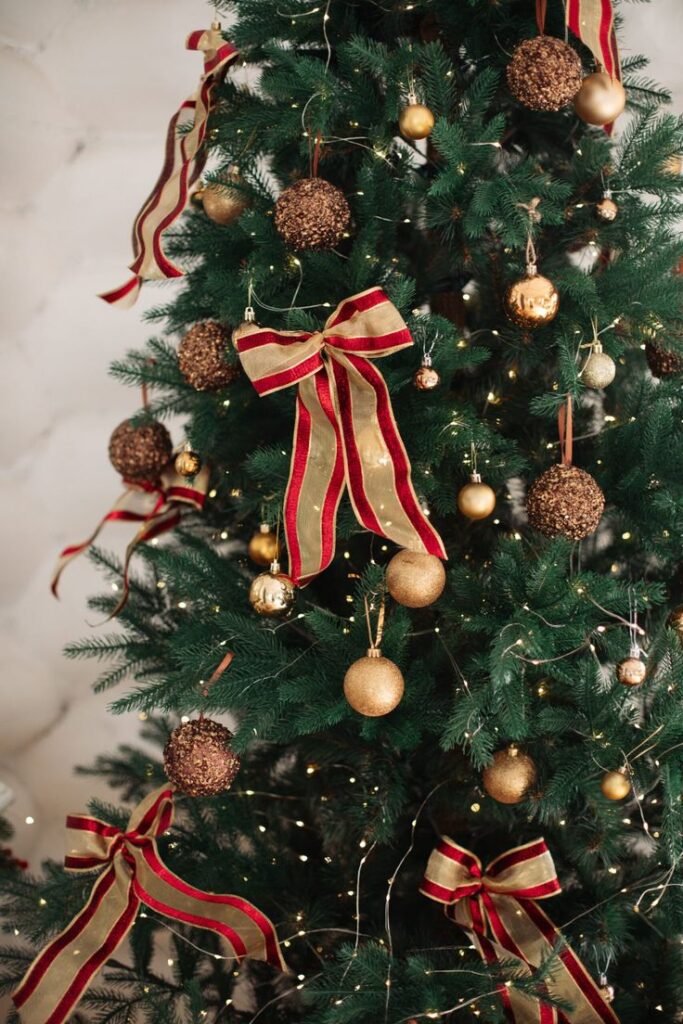 Festive Christmas tree adorned with gold baubles, red and gold ribbons, and lights, creating a holiday atmosphere.