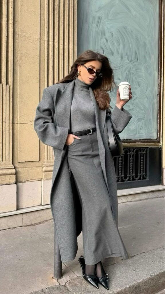 Woman in stylish gray ensemble poses with coffee outdoors. Fashion and urban lifestyle concept.