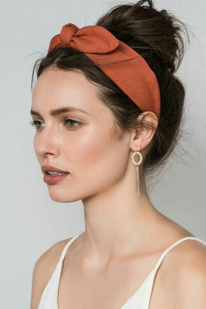 Woman wearing a rust headband, elegant hair updo, and gold hoop earrings in a minimalist style.
