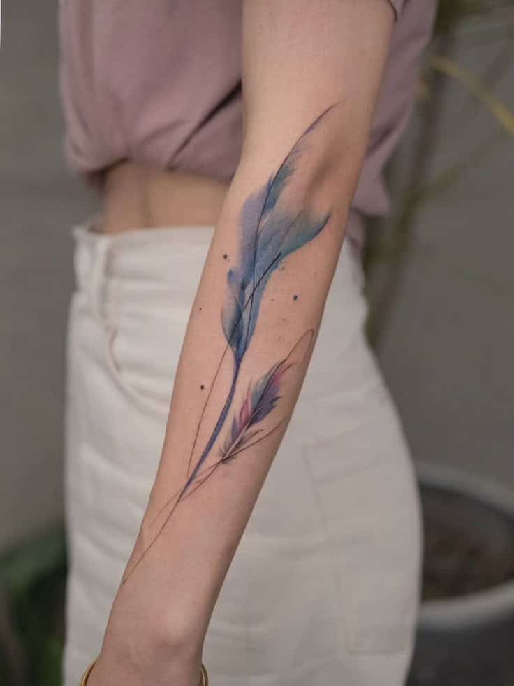 Watercolor feather tattoo on forearm, featuring blue and pink hues, showcasing delicate and artistic design.