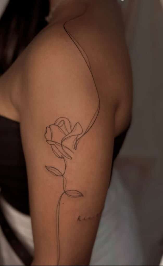 Minimalist rose line tattoo on a woman's arm, close-up, elegant floral design, black ink.