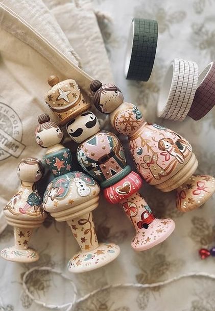Screenshot Hand-painted wooden dolls with intricate designs, lying on a surface, accompanied by decorative craft tapes in the background. | Sky Rye Design Hand-painted wooden dolls with intricate designs, lying on a surface, accompanied by decorative craft tapes in the background.