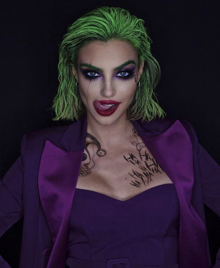 Person in bold makeup and green hair wearing a purple suit, showcasing a dramatic and artistic fashion look.