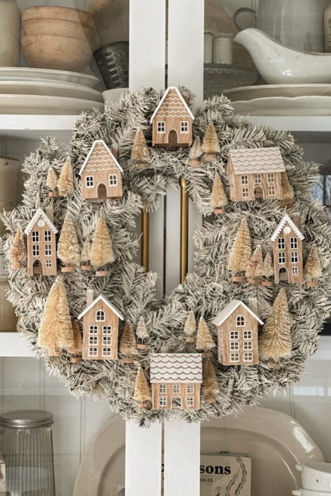 Festive wreath with mini houses and trees, perfect holiday decor on a cabinet door.