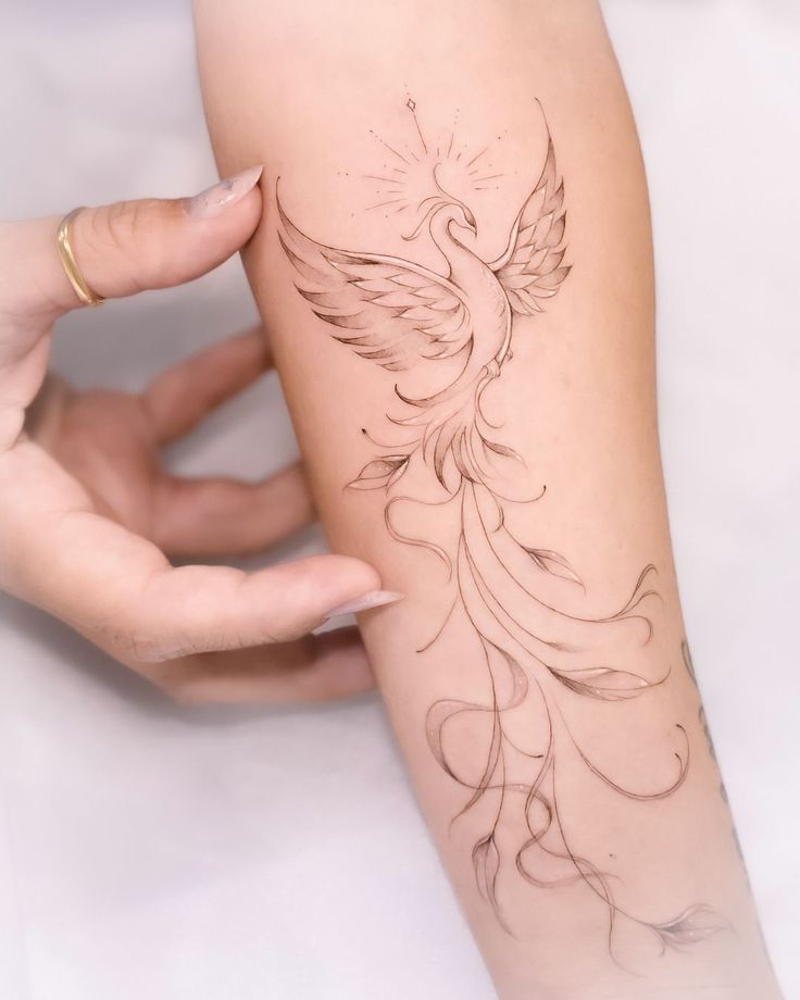Elegant phoenix tattoo with long, flowing tail on forearm, symbolizing rebirth and strength.