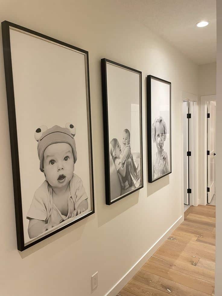 Black and white photo gallery in a hallway, showcasing three framed portraits on a light-colored wall with wooden flooring.