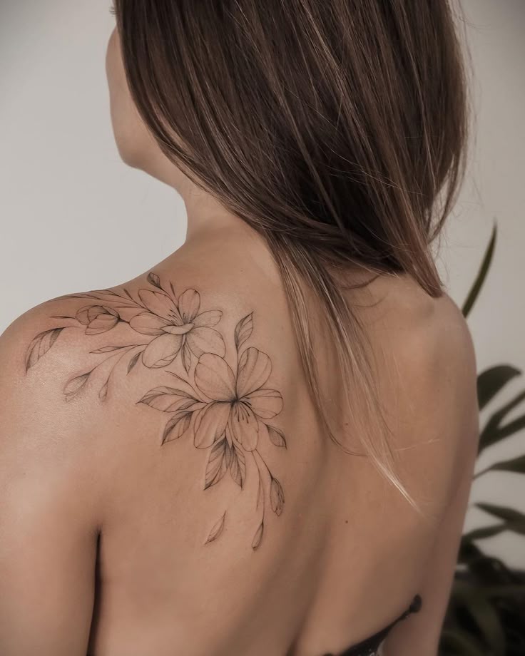 Woman's shoulder with a delicate floral tattoo design, showcasing elegant linework and blooming flowers.