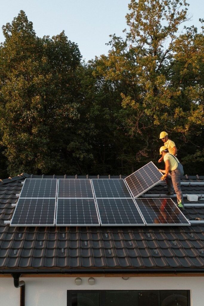 Workers installing solar panels on a rooftop surrounded by trees. Sustainable energy installation.