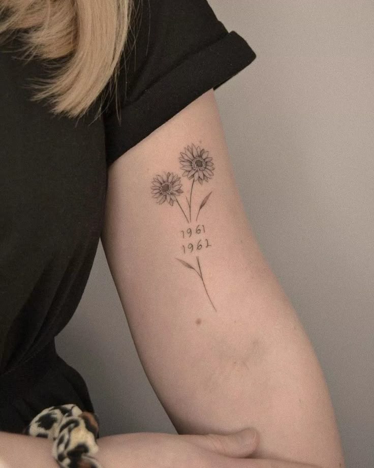 Minimalist floral tattoo with daisy design and years 1961, 1967 on forearm, symbolizing personal significance.
