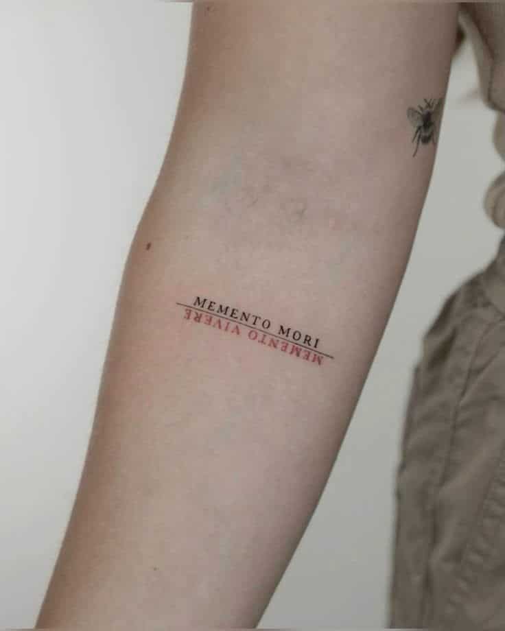 Forearm tattoo reads Memento Mori and Memento Vivere with a small bee nearby, symbolizing life and mortality.