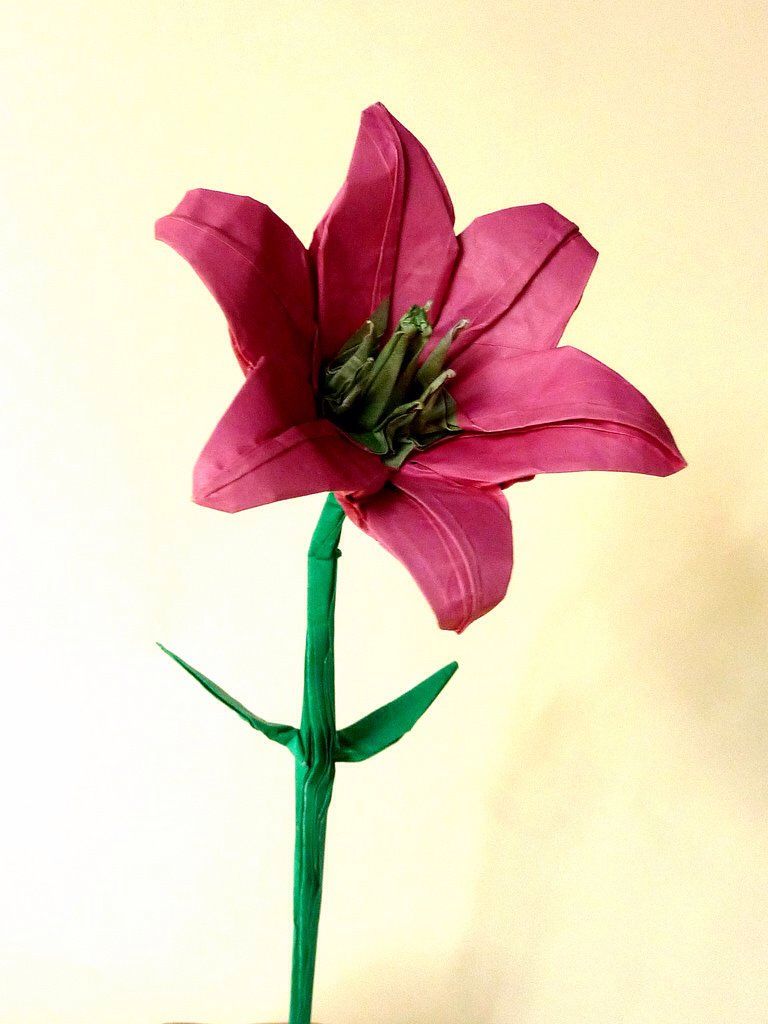 Origami flower crafted from pink and green paper, showcasing intricate folding on a light background.