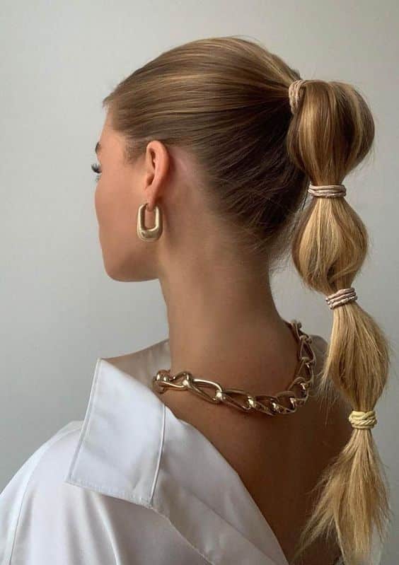 Elegant bubble ponytail hairstyle with gold accessories and a chic white blouse.