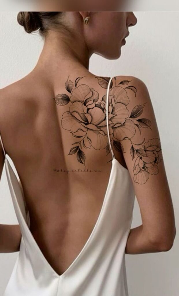 Back view of a woman with floral shoulder tattoo wearing a backless white dress.