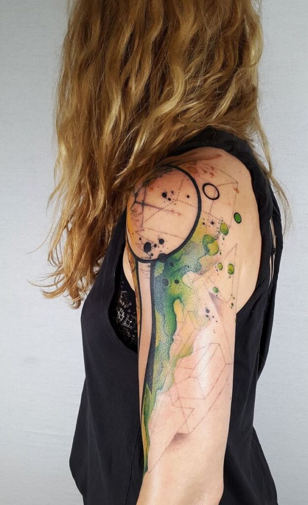 Abstract watercolor tattoo on woman's arm, featuring geometric shapes and vibrant colors.