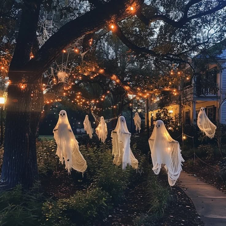 Ghost decorations hang from tree amidst Halloween lights and cobwebs in a spooky garden setting at dusk.