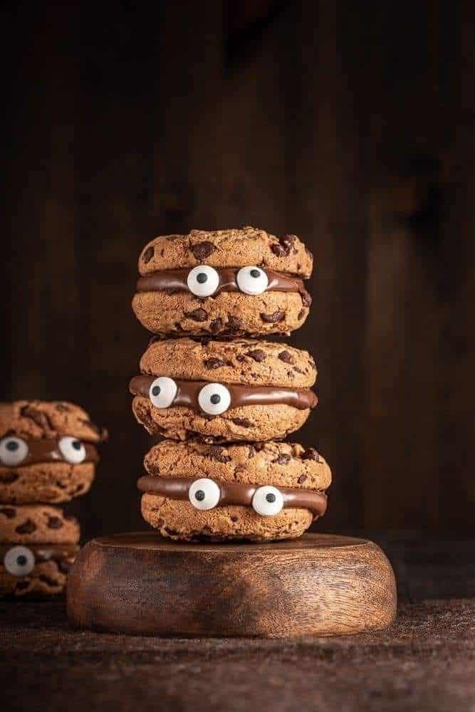 _ 13 Stacked chocolate chip cookies with googly eyes and chocolate filling, set on a wooden stand, playful dessert. | Sky Rye Design Stacked chocolate chip cookies with googly eyes and chocolate filling, set on a wooden stand, playful dessert.