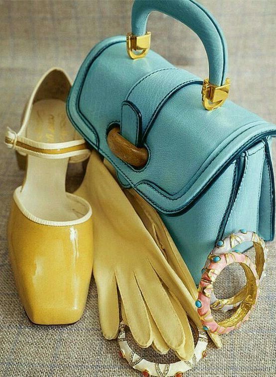 Stylish vintage accessories: blue handbag, yellow gloves, and shoes with colorful bracelets on a textured surface.