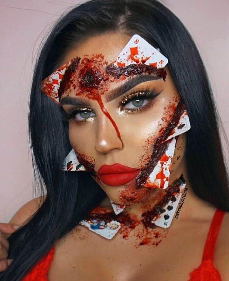 Woman with creative Halloween makeup featuring fake wounds and playing cards on face. Halloween