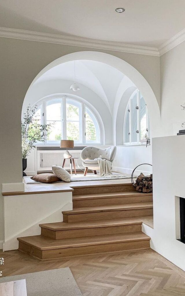 Cozy reading nook with arched windows, stylish chair, and neutral decor in a bright, serene interior space.