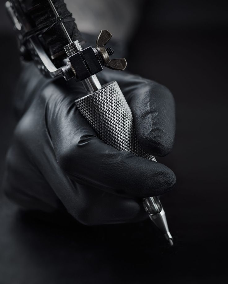 Close-up of tattoo artist holding a tattoo machine with black gloves, poised to create intricate designs.