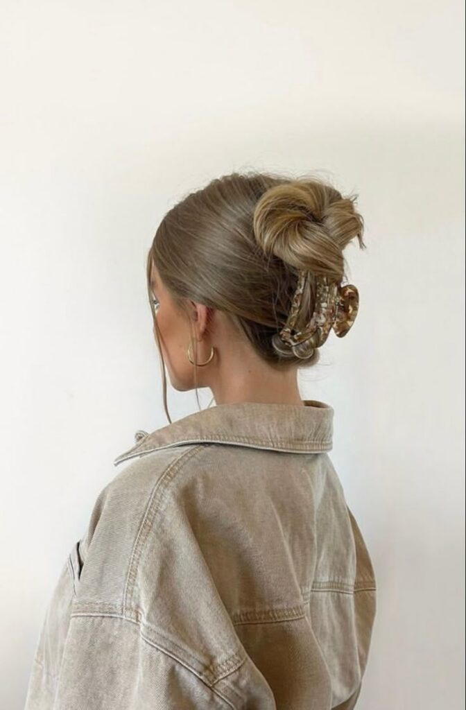 Woman in a brown jacket with a stylish updo using a decorative hair clip, viewed from the back.