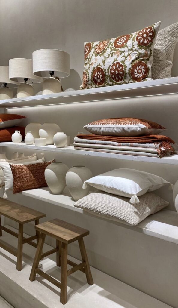 Decorative pillows and ceramic vases on shelves with wooden stools below, creating a cozy home decor display.