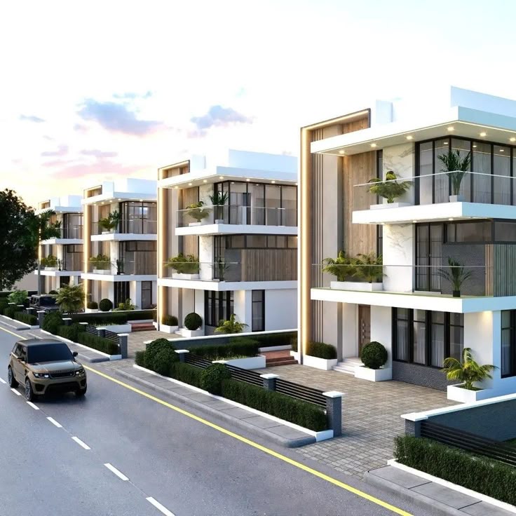 Modern townhouses with glass balconies and gardens along a tree-lined street at sunset.