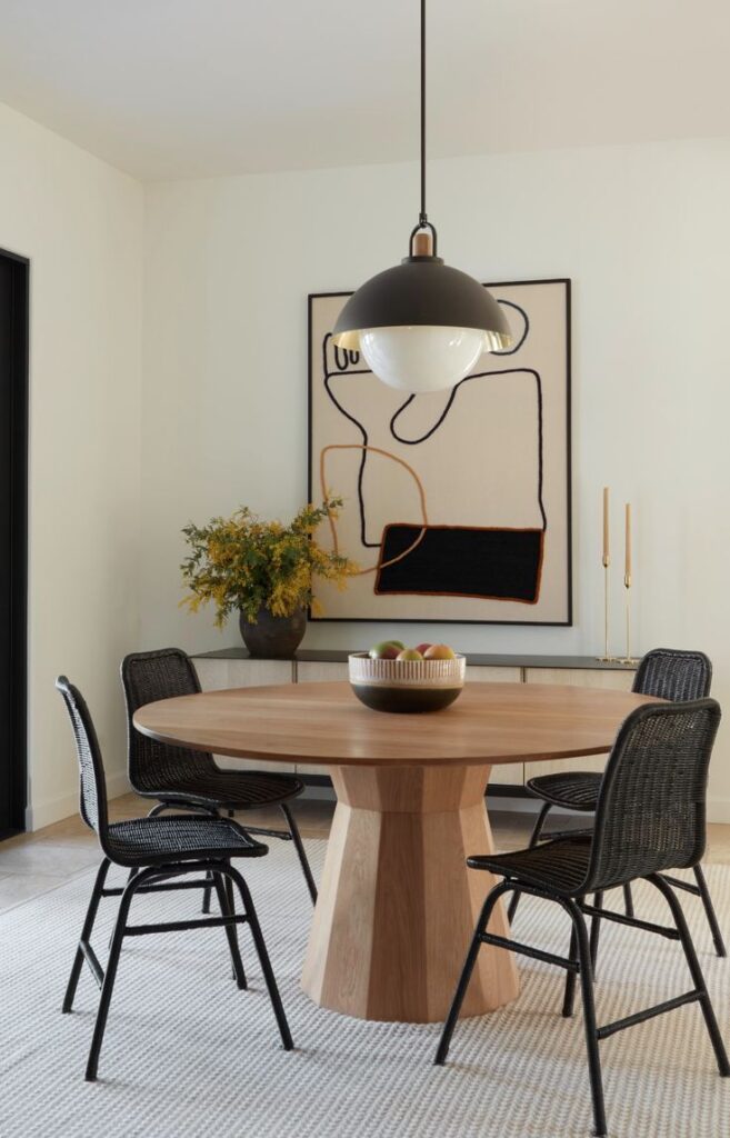 Modern dining room with wooden table, pendant light, abstract art, and black woven chairs. Minimalist decor and style.