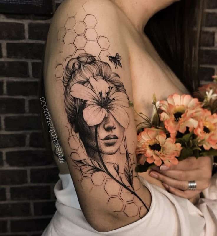 Tattoo of a woman's face with a flower, hexagon pattern, and bee on an arm, holding orange flowers.