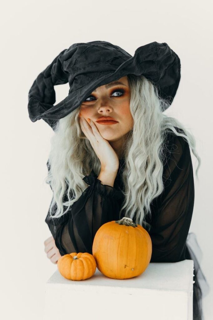 Woman in witch hat with pumpkins, celebrating Halloween in style.