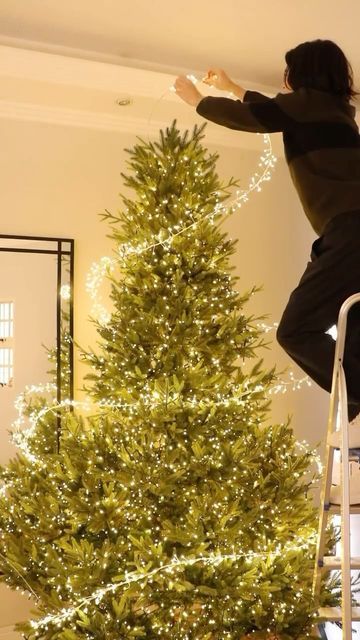 Person decorates a tall Christmas tree with string lights in a cozy living room, creating a festive holiday atmosphere.