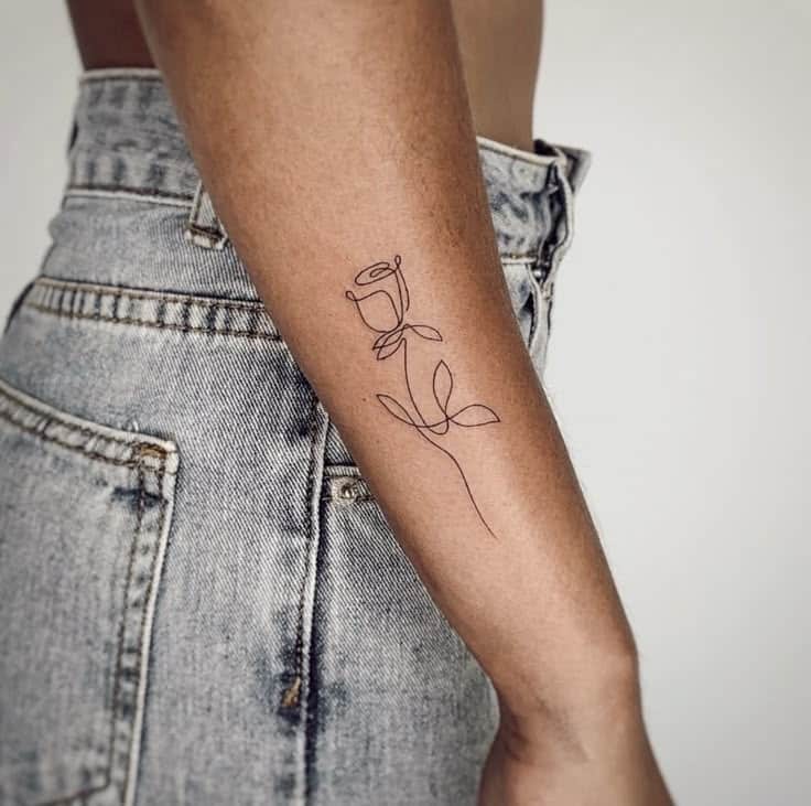 Minimalist rose line tattoo on forearm, person wearing blue jeans.