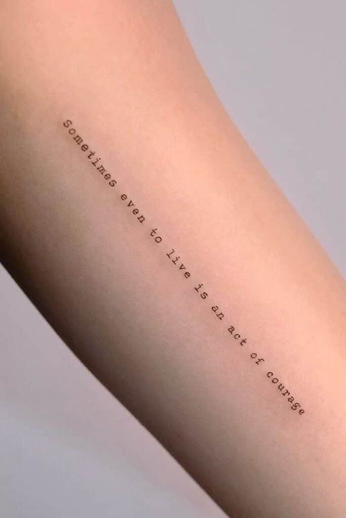 Tattoo on forearm with motivational quote about courage in life. Minimalist black ink design on skin.