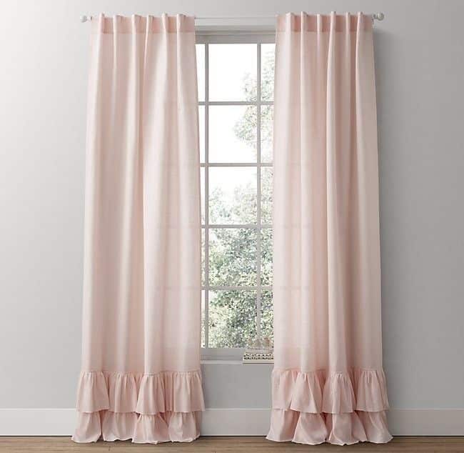 Soft pink ruffled curtains hanging over a window, enhancing room ambiance and decor with elegance and style.